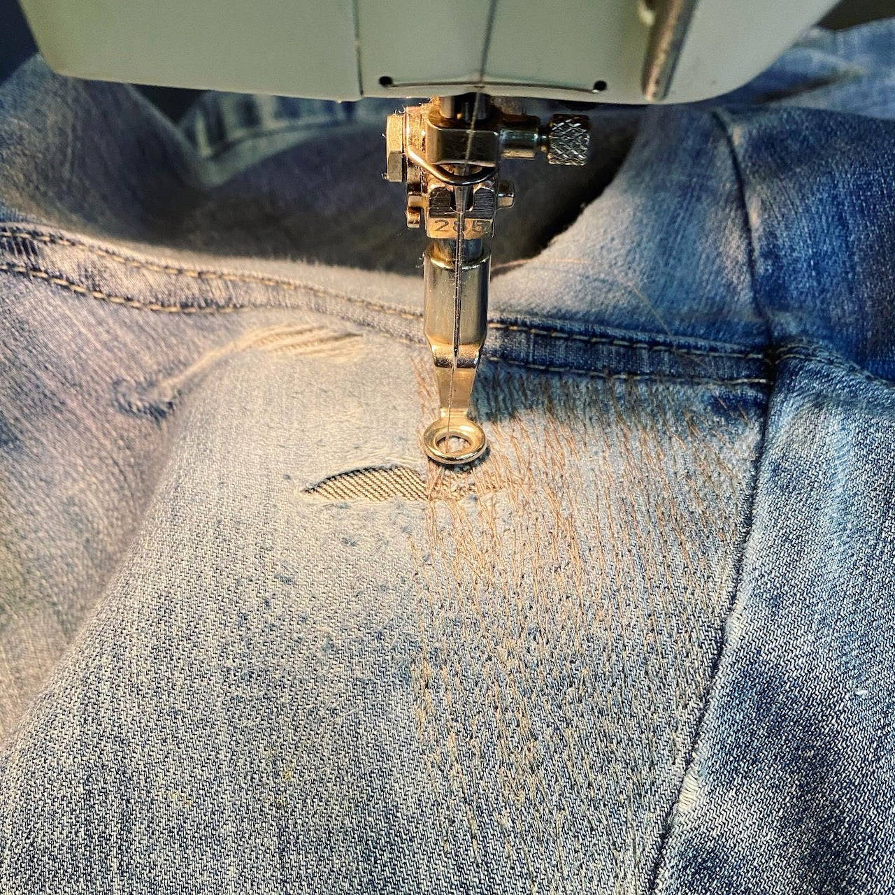 A pair of jeans is being mended with a sewing machine.